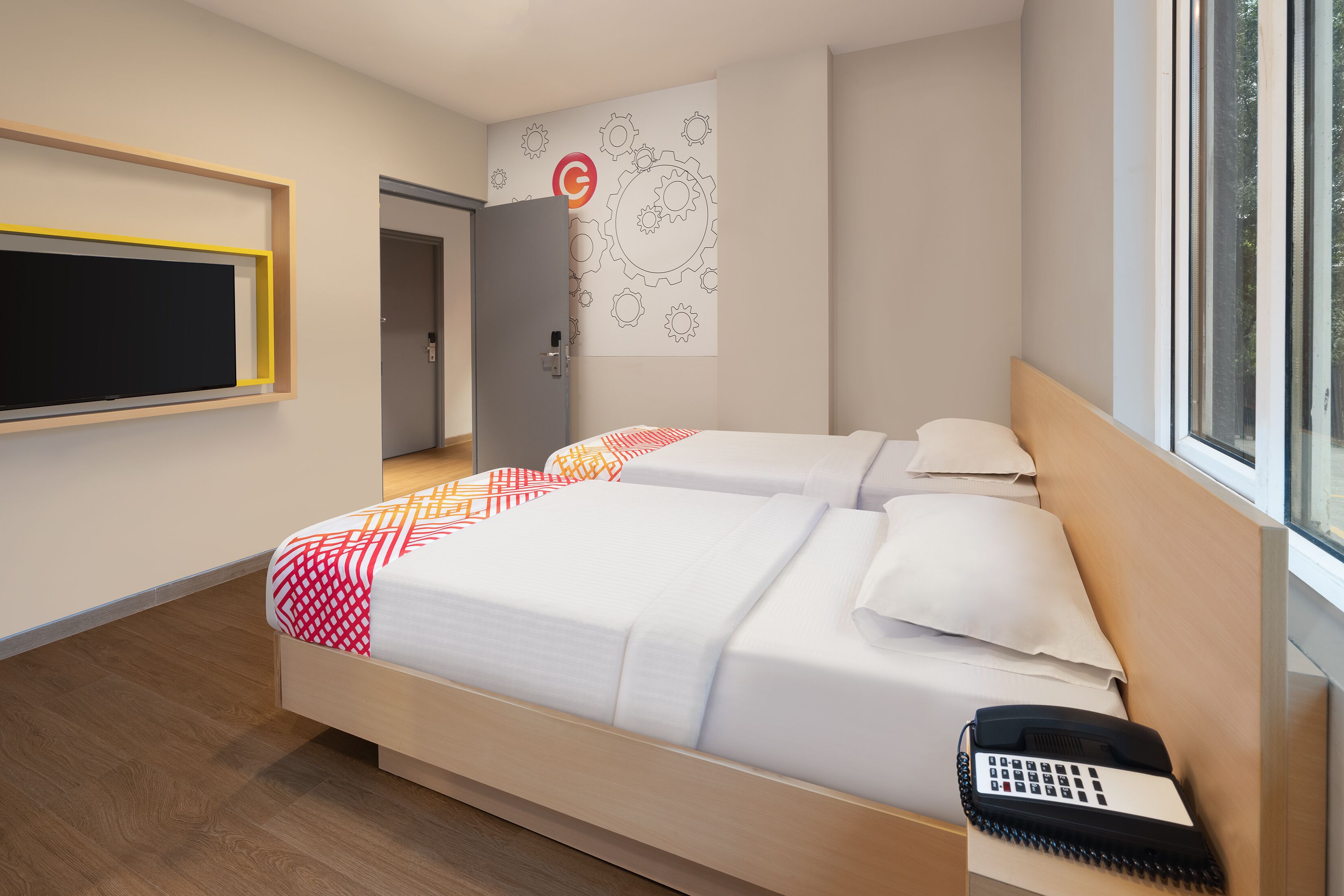 A modern hotel room with a large bed, a bedside telephone, and a window with a view of trees.