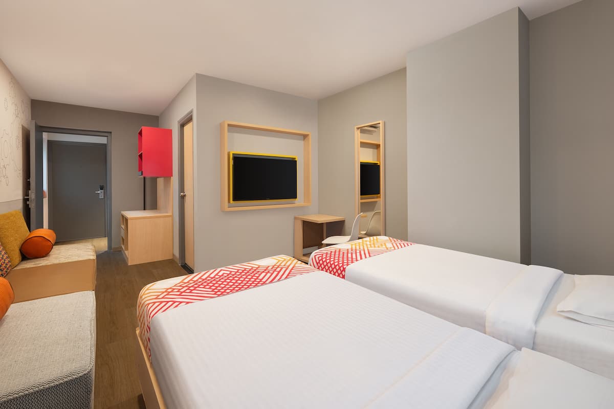 A hotel room with two beds, a desk, a chair, a TV, and a wardrobe.