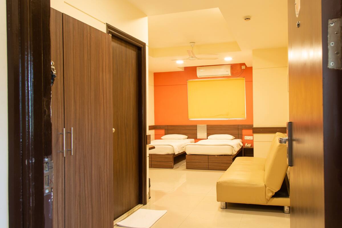 A hotel room with a wooden wardrobe, a bed with two pillows, a bedside table, and a small table with a bowl.