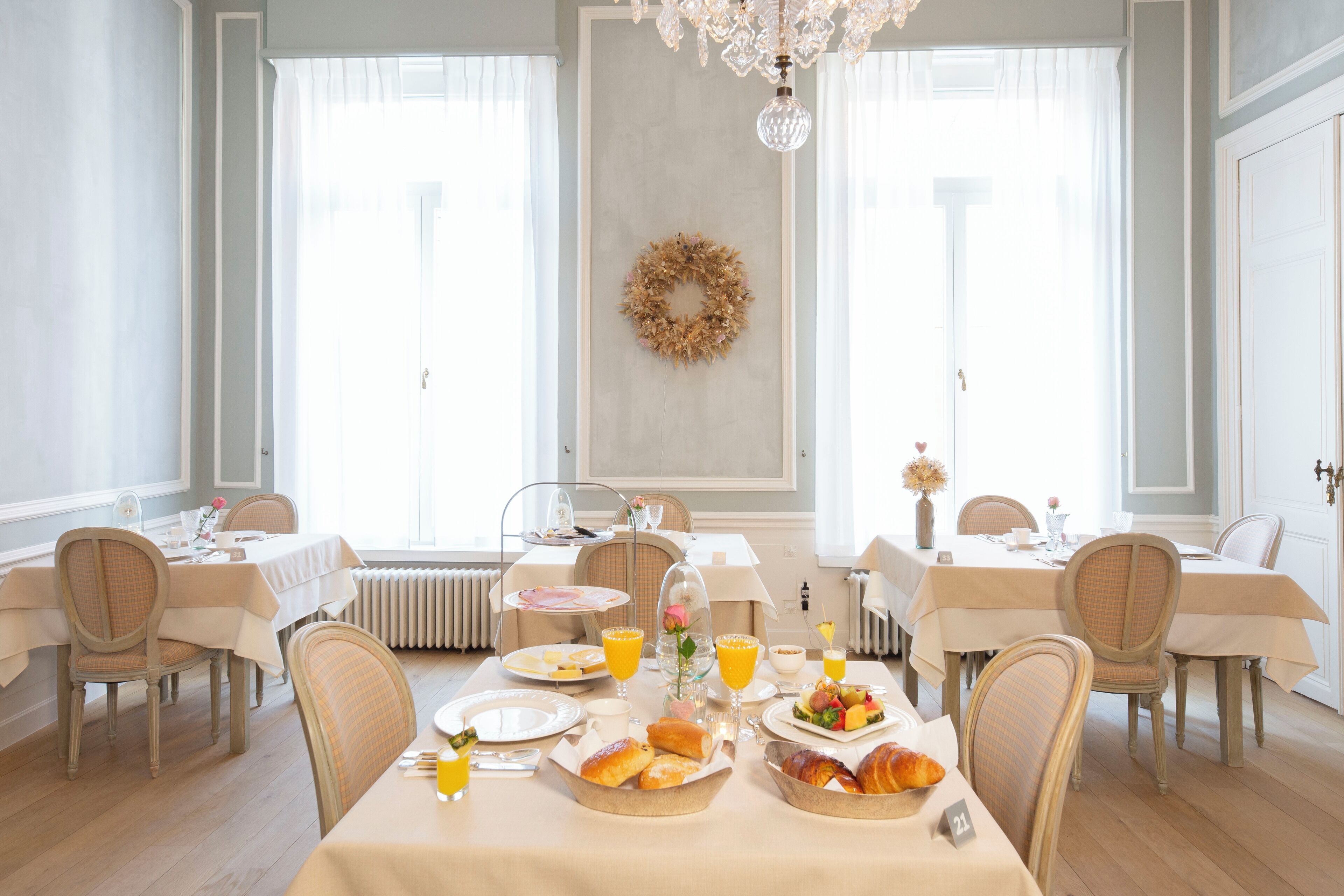 Uma sala de jantar luminosa com duas mesas preparadas para o café da manhã, com pão, doces e frutas.
