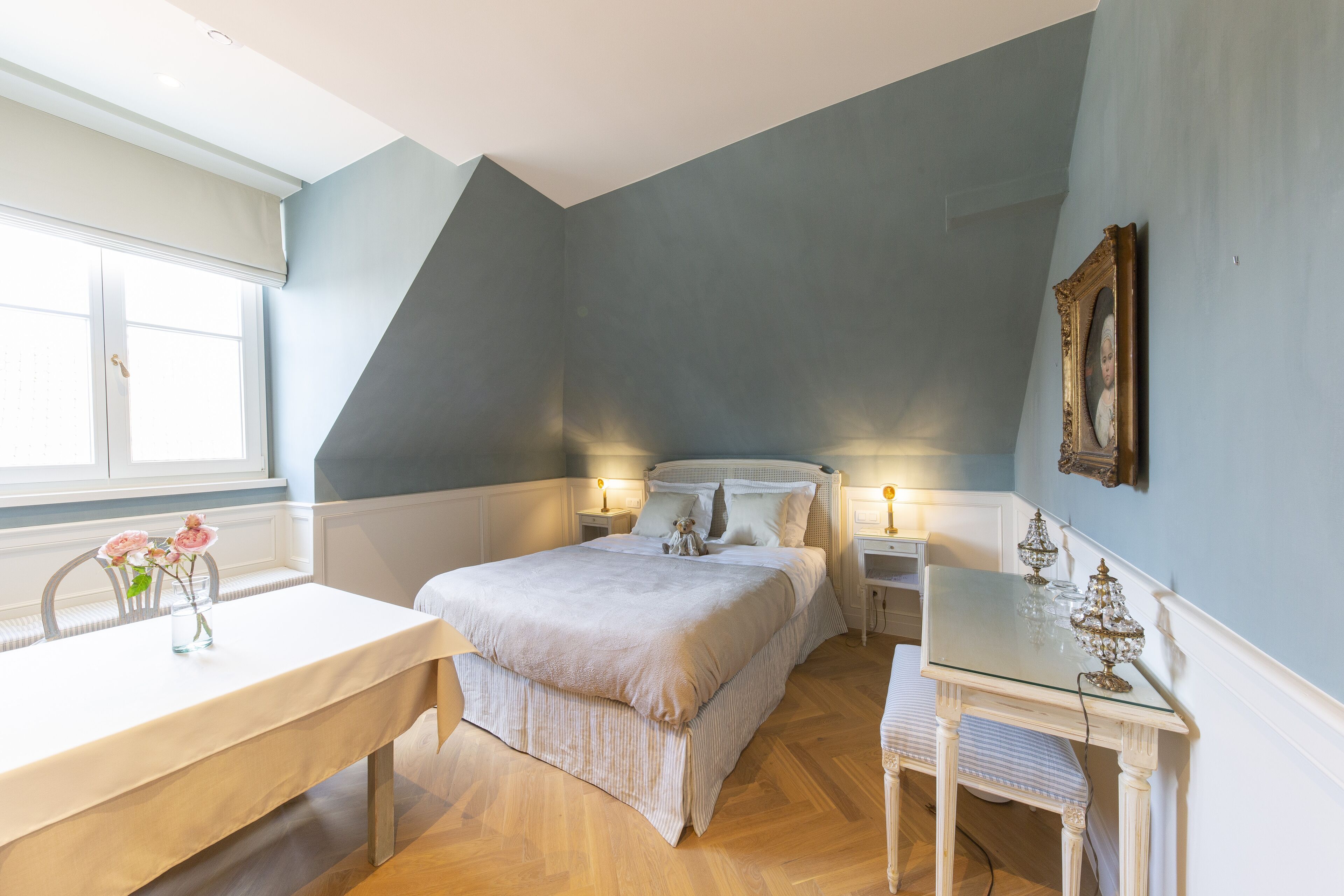 Quarto com cama, mesas de cabeceira, escrivaninha e janela.