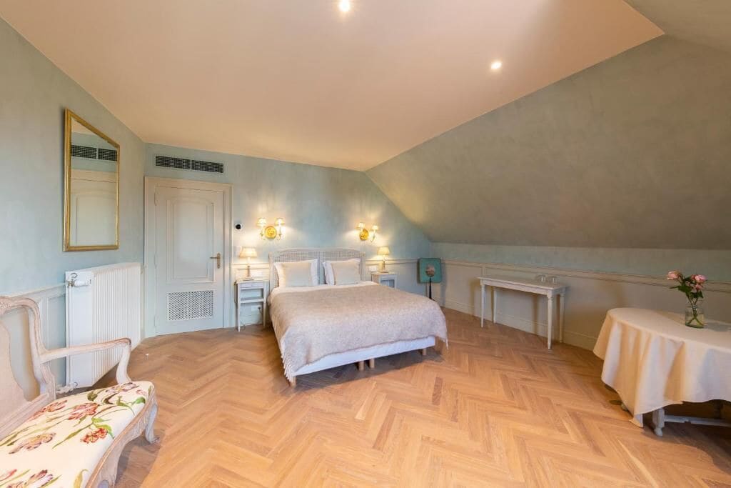 A bedroom with a bed, bedside tables, a chair, a small table with a vase, and a mirror on the wall.