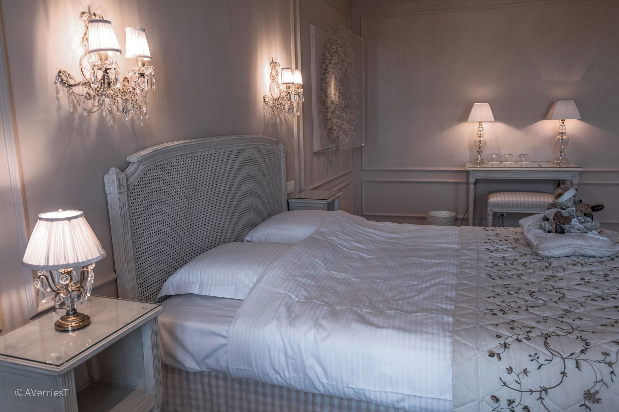 A bedroom with a large bed, two bedside lamps, a nightstand, and a small table with a lamp.