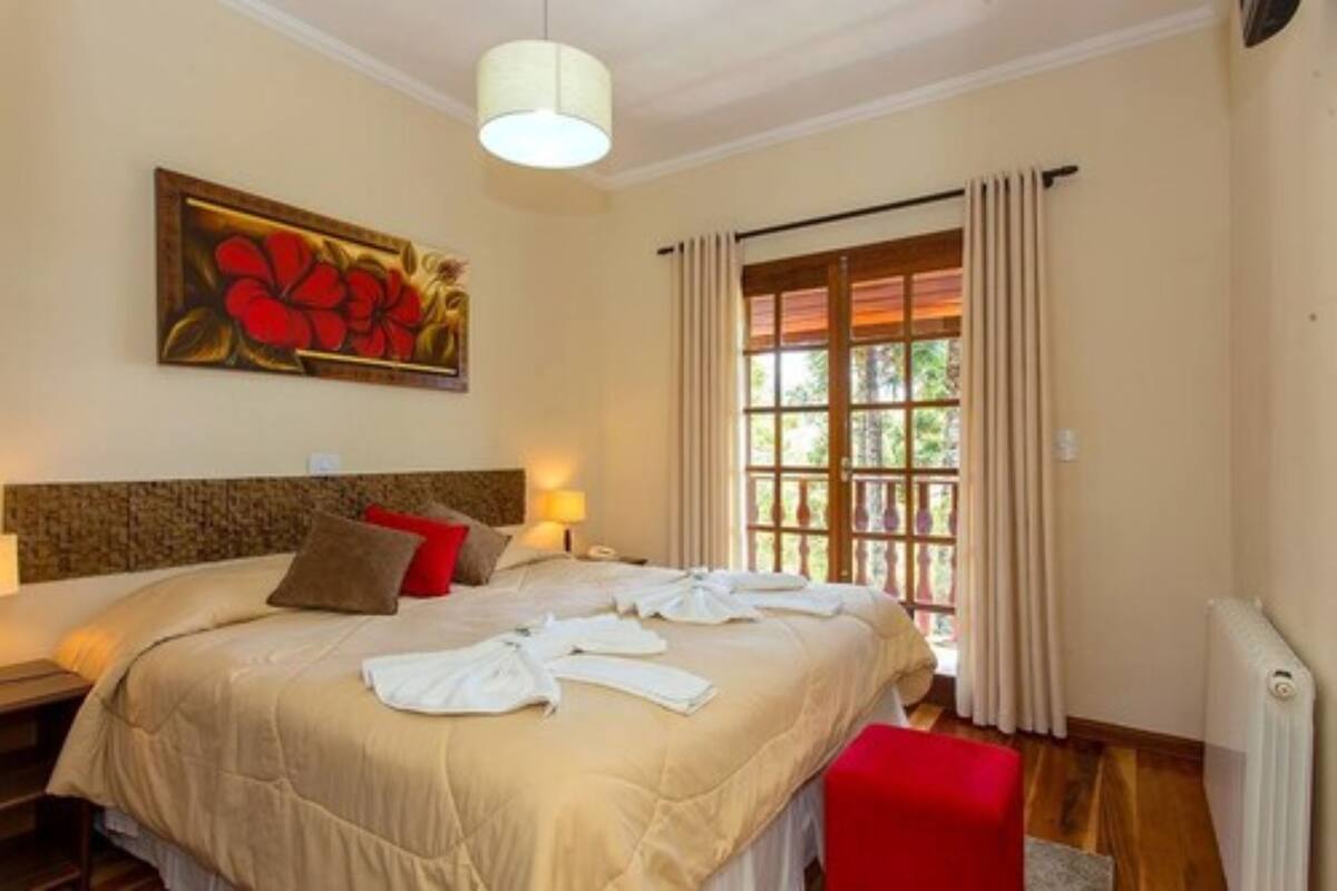 A hotel room with a large bed, a painting of flowers on the wall, a window with curtains, and a radiator.