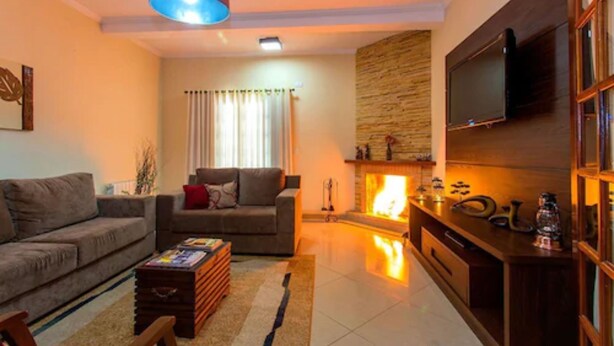 A living room with a fireplace, a sofa, a coffee table, and a television mounted on the wall. - Pousada Serra do Jordão (Campos do Jordão)