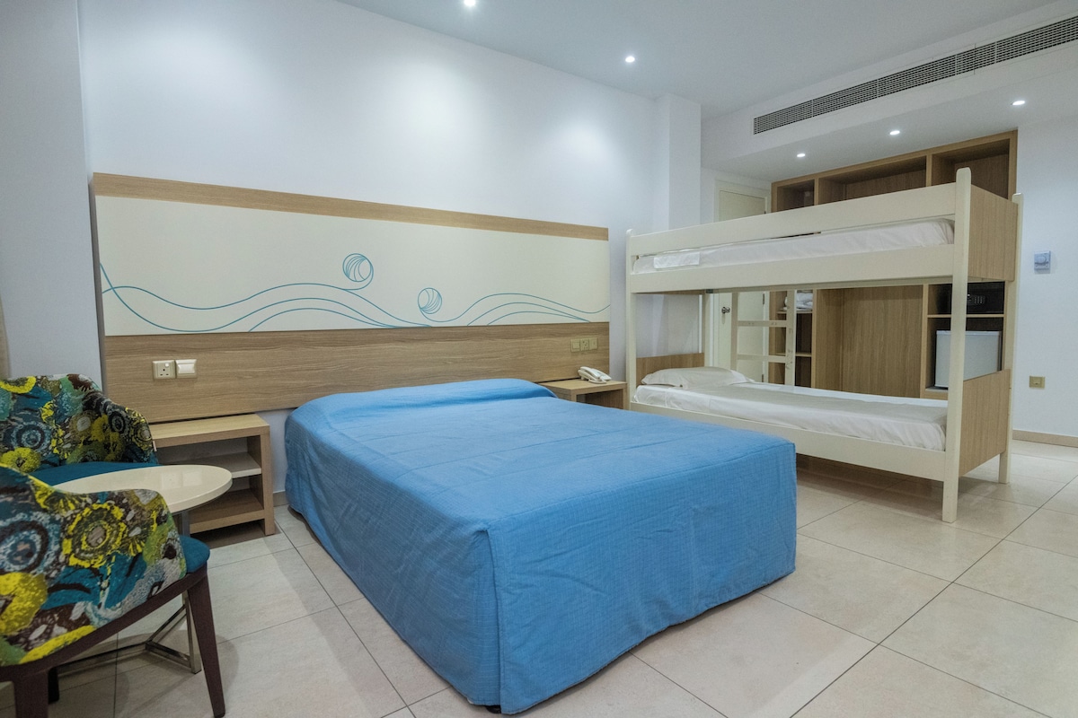 Una habitación de hotel con literas, una cama individual, un escritorio con silla y un adorno en la pared.