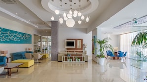 A modern hotel lobby with a central seating area, a large TV screen, and a variety of seating options including sofas and chairs. - Stamatia Hotel (Ayia Napa)