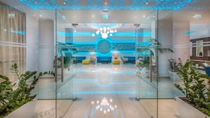A modern lobby with glass walls, a blue seating area, and a central decorative light fixture. - Stamatia Hotel (Ayia Napa)