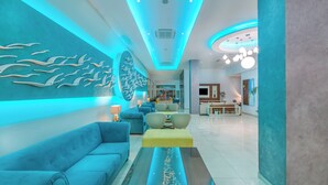 A modern living room with a blue sofa, a yellow ottoman, and a wall with a dolphin mural. - Stamatia Hotel (Ayia Napa)