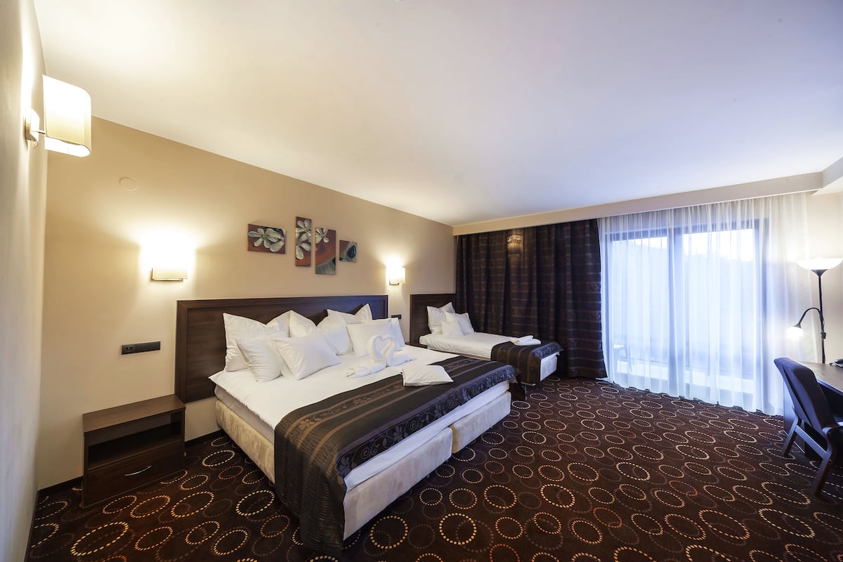 Habitación de hotel con dos camas, un escritorio y un ventanal grande con cortinas.