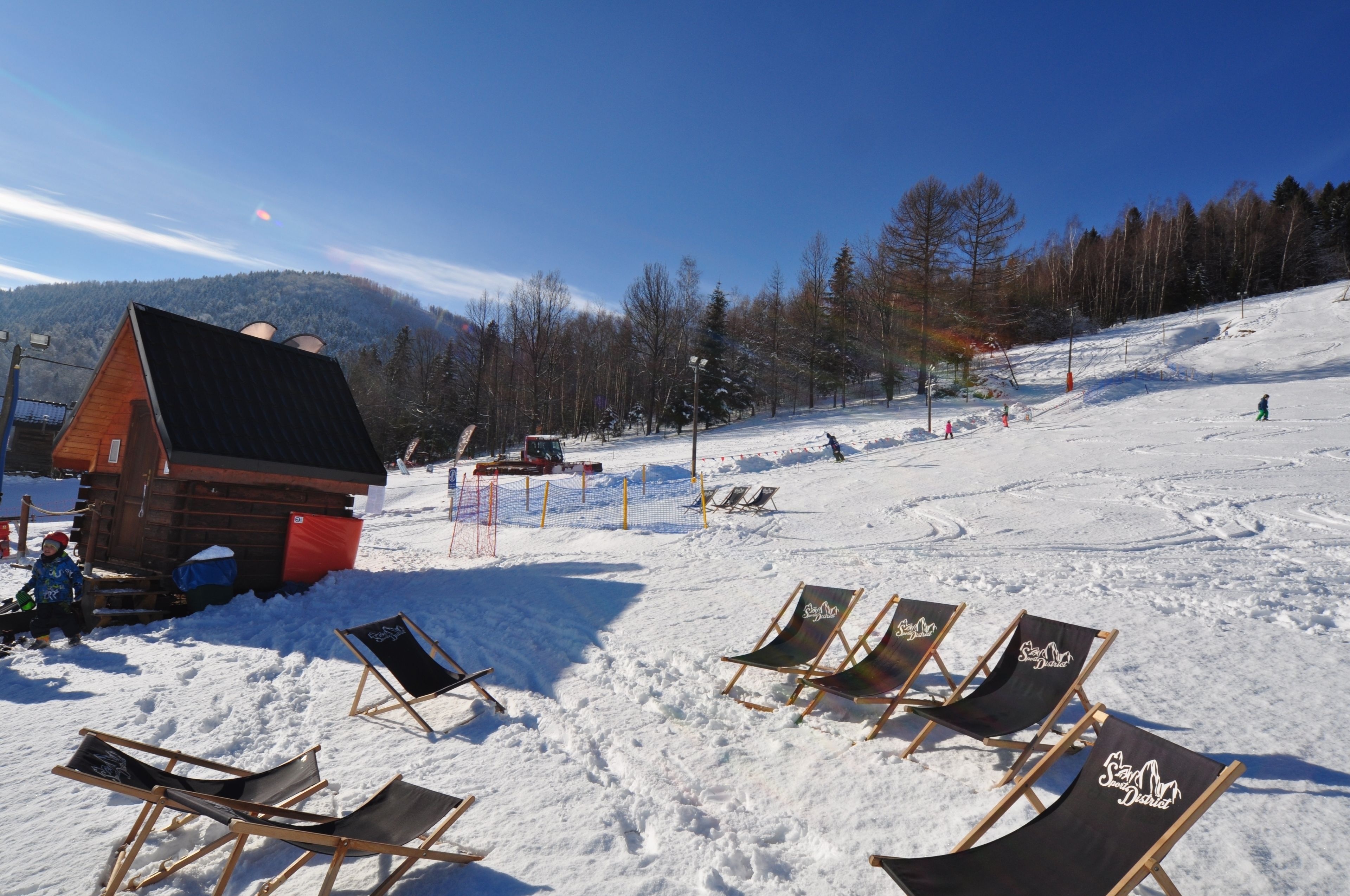 Pista de esquí nevada con sillones de descanso y una cabaña de madera.