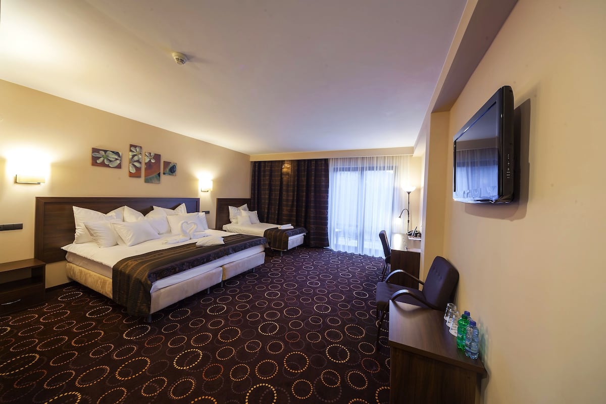 Habitación de hotel con una cama grande, dos mesitas de noche, un escritorio con sillas, un televisor de pantalla plana y una ventana con cortinas.
