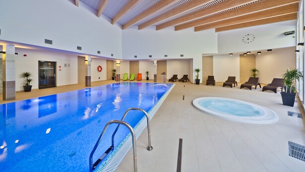 Een binnenzwembad met houten plafond, ligbedden en een jacuzzi.