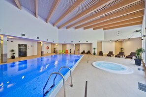 Une piscine intérieure avec un plafond en bois, des chaises longues et un jacuzzi.