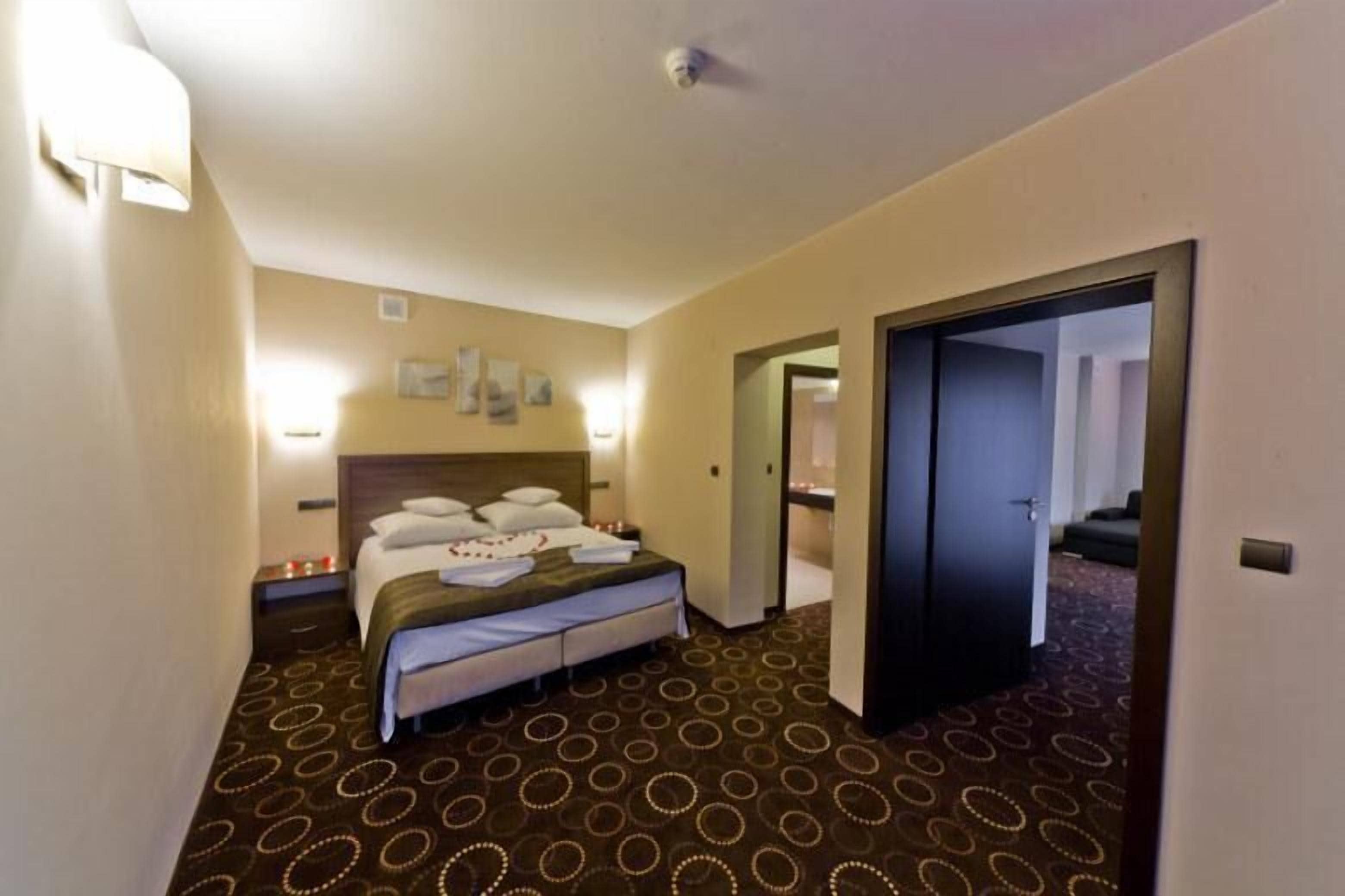 Een hotelkamer met een bed, nachtkastjes, een vloerbedekking en een deur naar een andere kamer.