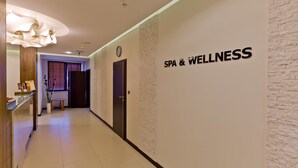 A hallway with a sign reading "SPA & WELLNESS" on the wall, a reception desk, and a modern light fixture.