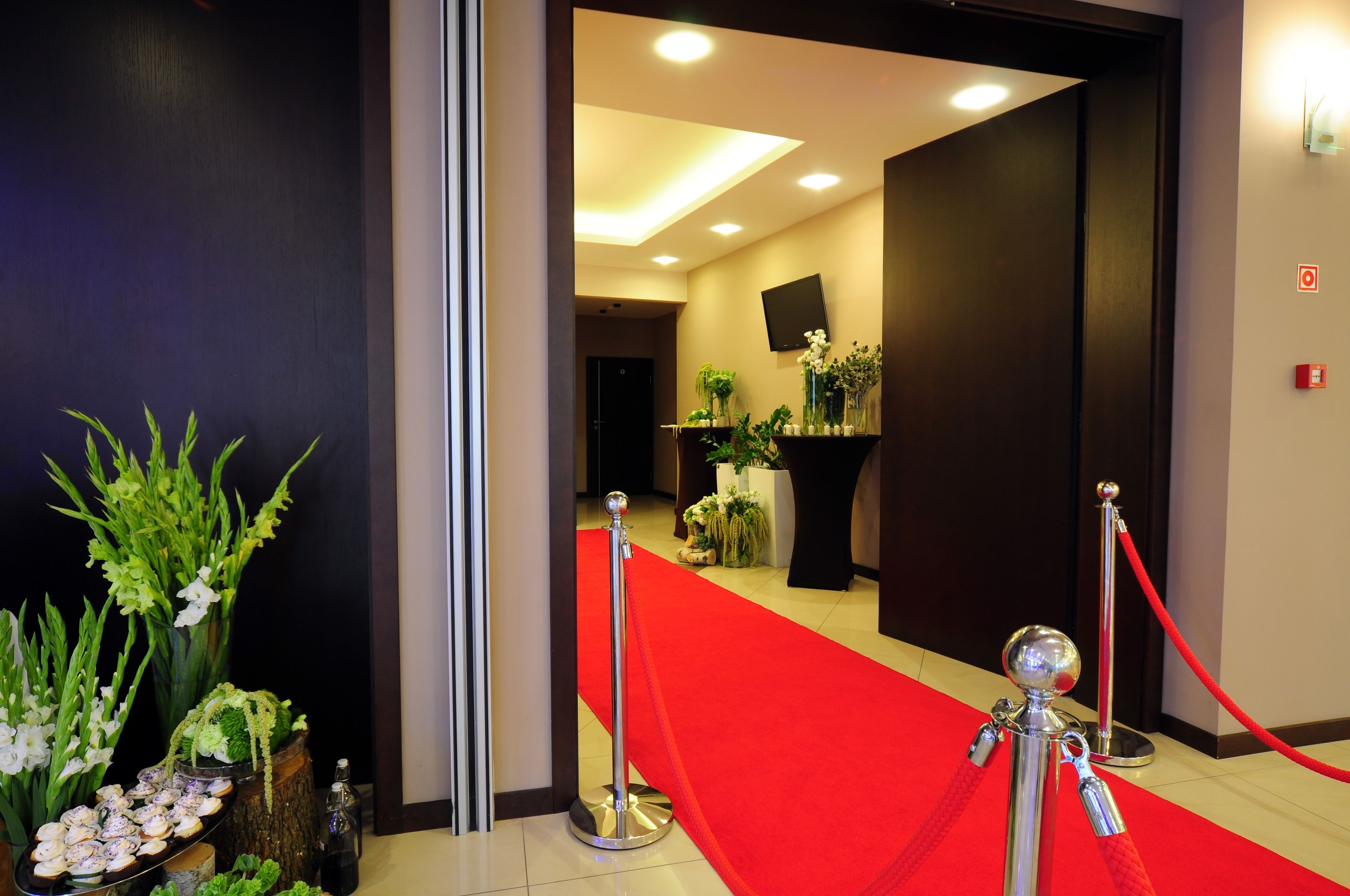 Un vestíbulo de hotel con alfombra roja, plantas en macetas y un televisor de pantalla plana en la pared.