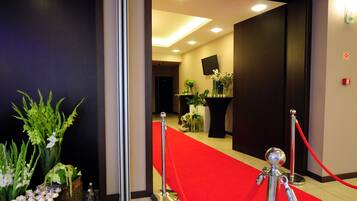 Un vestíbulo de hotel con alfombra roja, plantas en macetas y un televisor de pantalla plana en la pared.