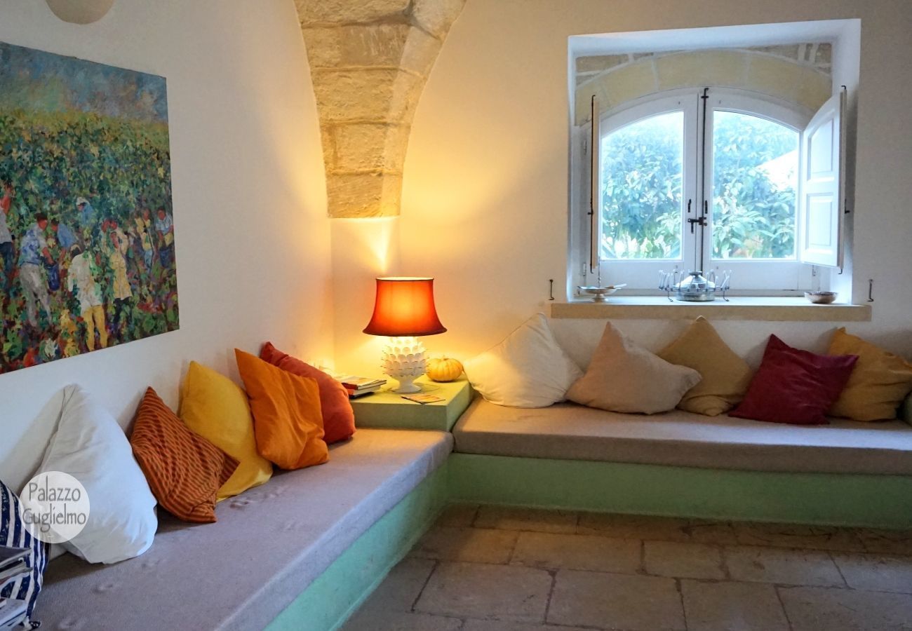Un coin salon confortable avec des coussins, une table avec une lampe et une fenêtre donnant sur un paysage verdoyant.