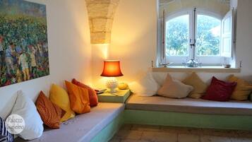 Un coin salon confortable avec des coussins, une table avec une lampe et une fenêtre donnant sur un paysage verdoyant.