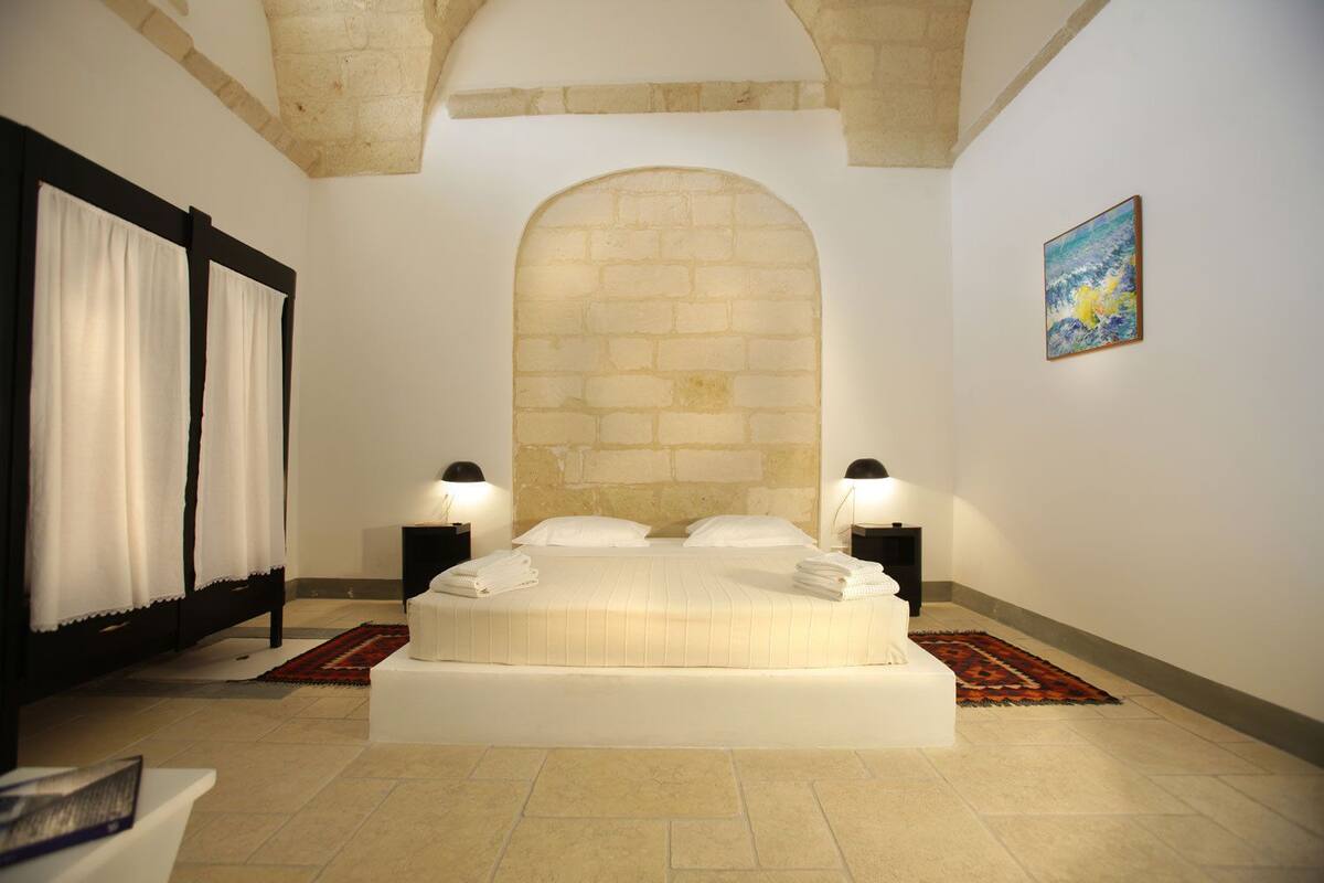 Un dormitorio con una cama grande, dos mesitas de noche con lámparas, un cuadro en la pared y un arco de piedra sobre la cama.