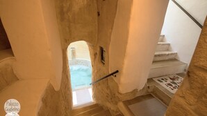 A stone-walled bathroom with a bathtub, a towel rack, and a view of a pool. - Palazzo Guglielmo Albergo Diffuso (Ortelle)