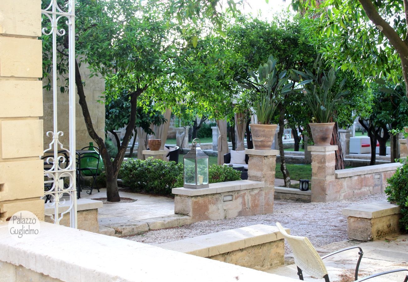 A courtyard with stone benches, potted plants, and a wrought iron fence.