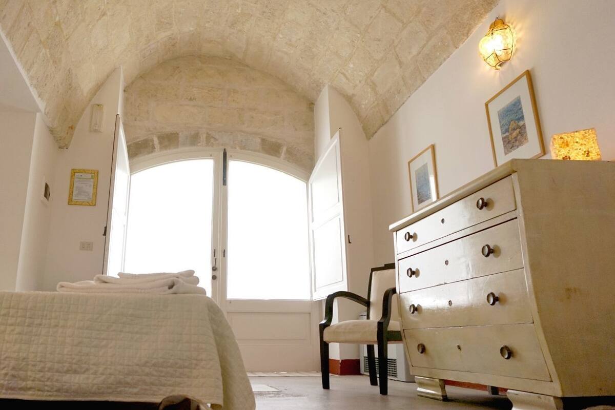 Un dormitorio con cama, cómoda, silla y ventana con cortinas.