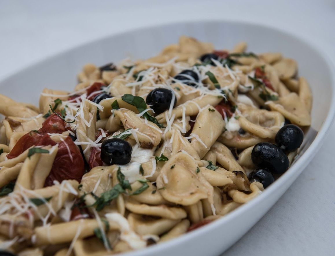 A bowl of pasta with cheese, black olives, and tomatoes.