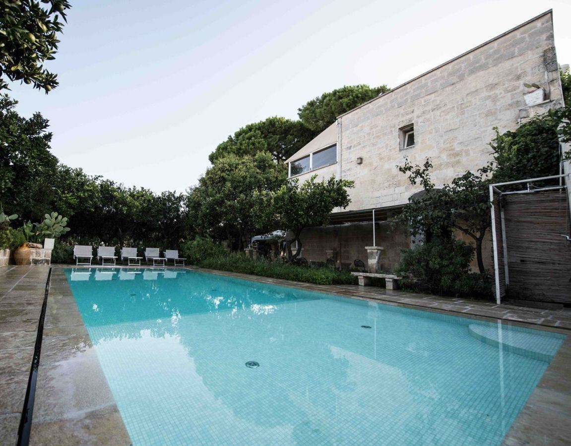 A swimming pool with lounge chairs, surrounded by trees and a stone building.