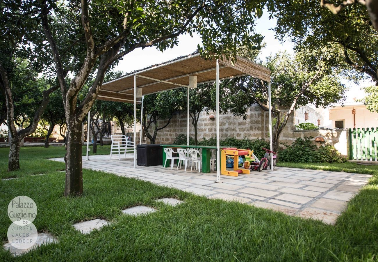 Een terras buiten met een overdekte zithoek, een speelconstructie en een stenen muur op de achtergrond.