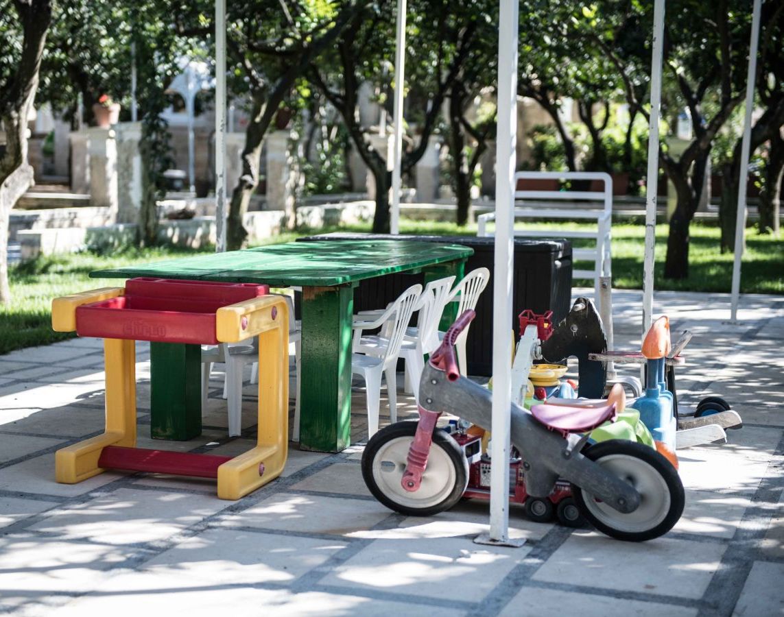 Zona de juegos infantiles con una pequeña mesa y sillas, un tractor de juguete y una estructura de juego verde.