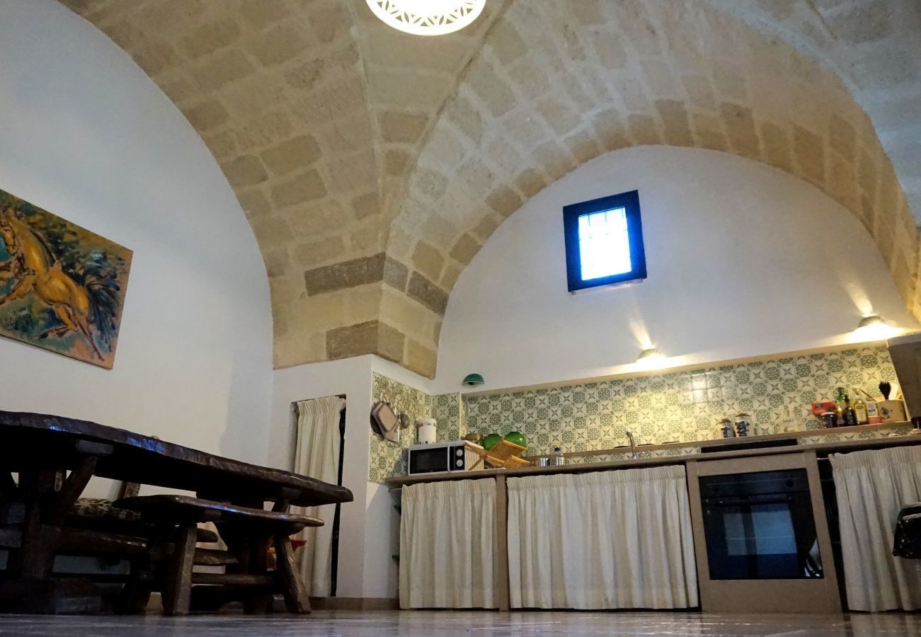 A rustic kitchen with stone walls, a wooden dining table, and a small window.