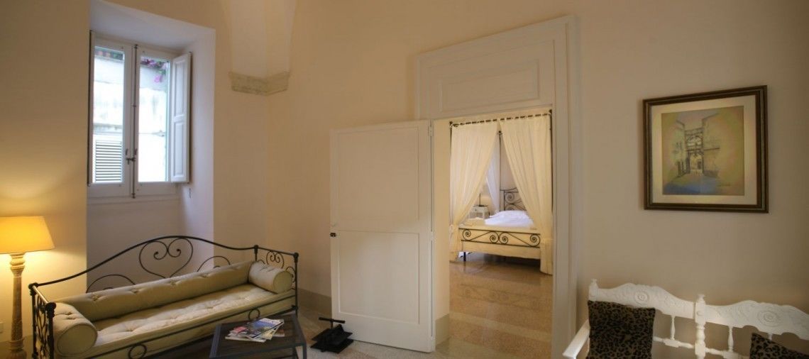 A bedroom with a bed, a window, a door, and a painting on the wall.