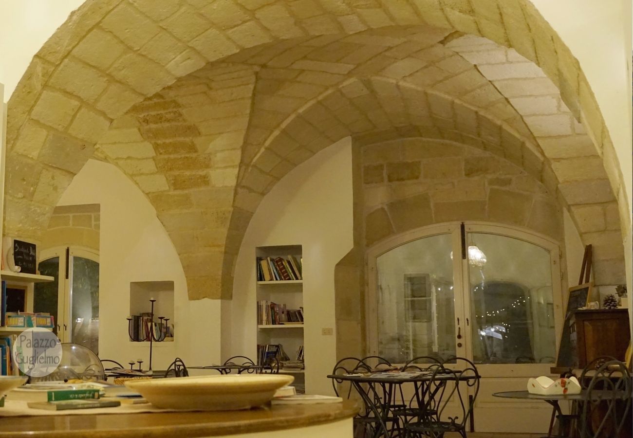 Un intérieur chaleureux avec un plafond en forme d’arc en pierre, un coin repas avec des chaises en métal et une bibliothèque remplie de livres.
