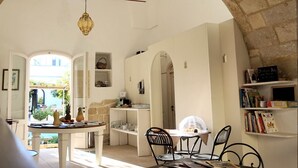 A dining area with a table and chairs, a hanging light fixture, and a view through an archway. - Palazzo Guglielmo Albergo Diffuso (Ortelle)