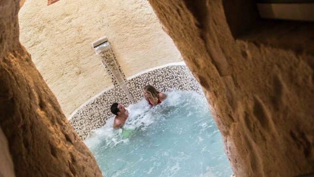 A stone-walled hot tub with two people, a tiled floor, and a small window with a light fixture. - Palazzo Guglielmo Albergo Diffuso (Ortelle)