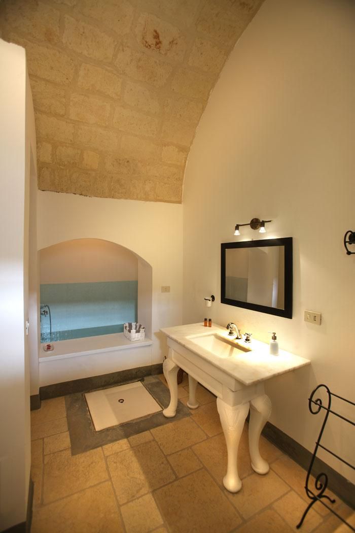 Un baño con tocador blanco, un espejo grande, una bañera y una pared de piedra.