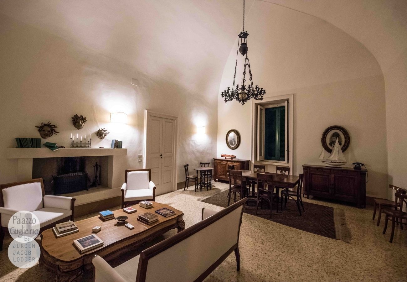 A spacious living room with a fireplace, a chandelier, and a dining area with wooden furniture.