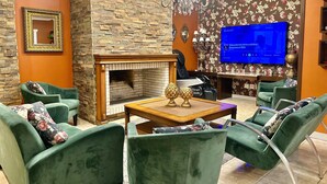 A modern living room with green upholstered sofas, a fireplace, a television, and a chandelier. - Hotel Glamour da Serra (Gramado)