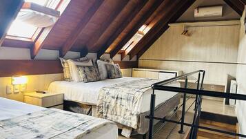 Una habitación con techo inclinado, dos camas con ropa de cama a juego, una mesita de noche con lámpara y un radiador.