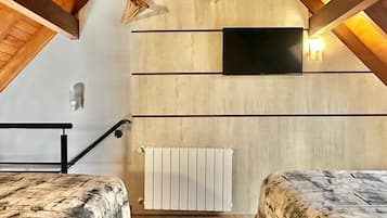 Quarto com teto inclinado, televisão montada na parede, radiador e cama com cobertura estampada.
