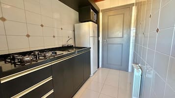 Una cocina con estufa a gas, gabinetes negros, un refrigerador blanco y una puerta con panel decorativo.
