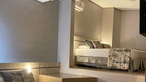 A modern bedroom with a large bed, a headboard, a flat-screen TV mounted on the wall, and a staircase leading to an upper level. - Hotel Glamour da Serra (Gramado)