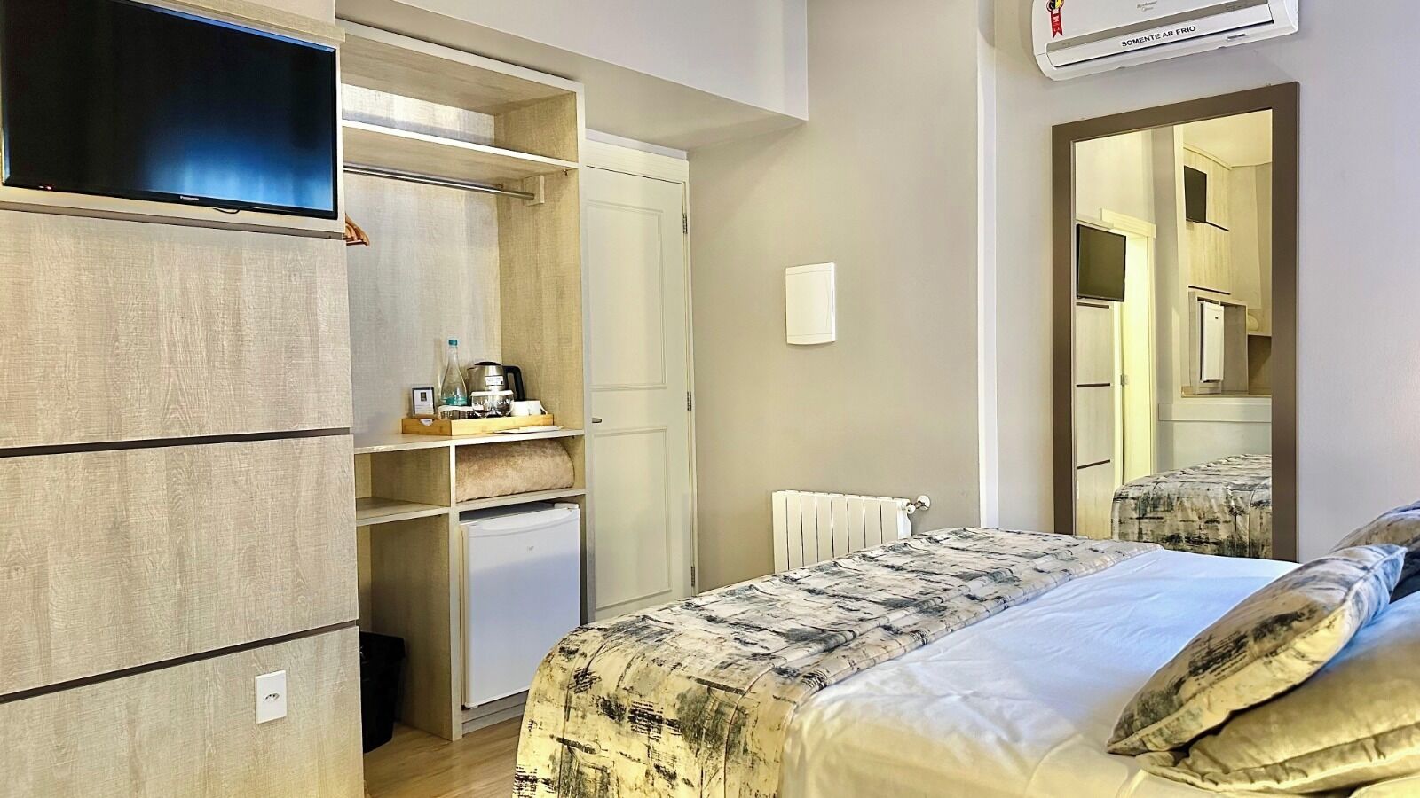 A bedroom with a bed, a wardrobe, a small kitchenette, and a mirror.