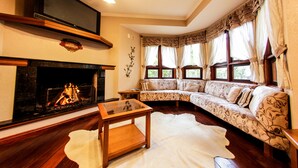 A living room with a fireplace, a sofa, a TV, and a glass coffee table. - Pousada das Papoulas (Gramado)