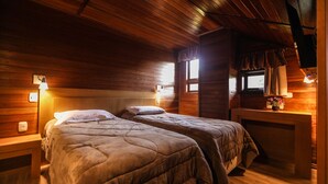 A cozy cabin-style room with two beds, wooden walls, and a fireplace. - Pousada das Papoulas (Gramado)