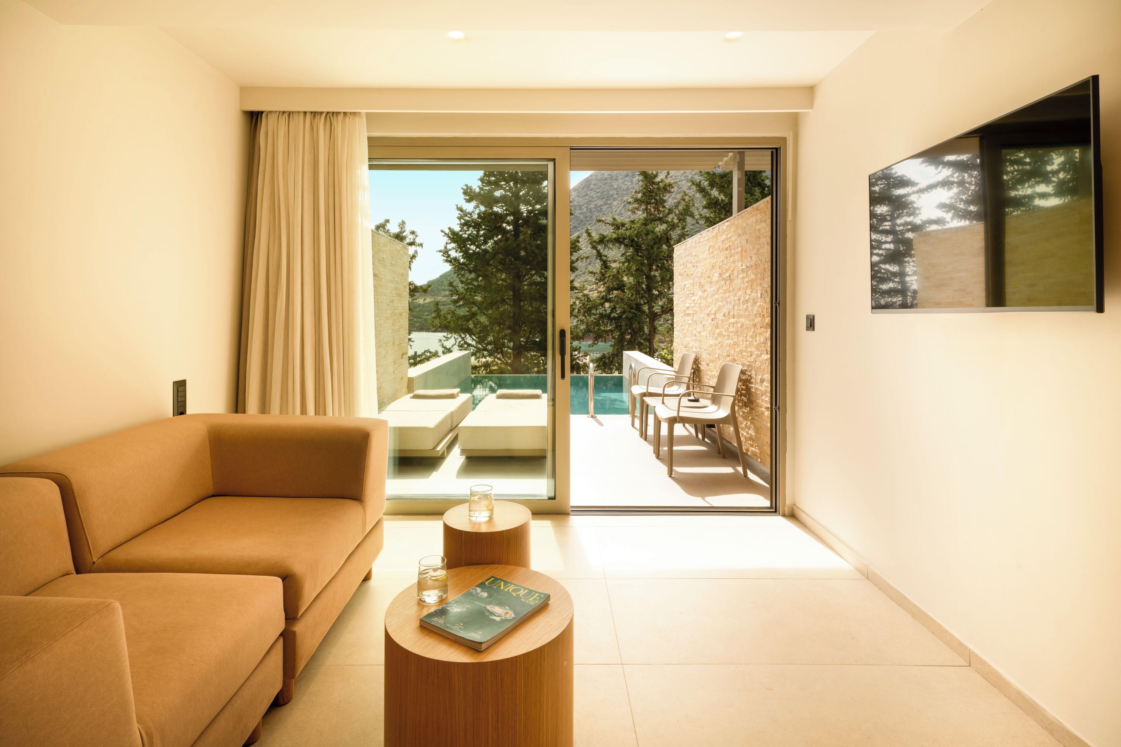 A modern living room with a sofa, a coffee table, and a sliding glass door leading to an outdoor seating area.