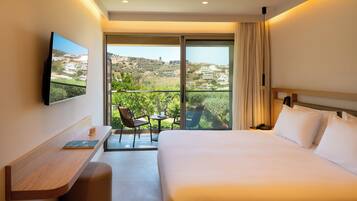 A hotel room with a bed, a desk, a chair, a TV, and a balcony with a view of the landscape.