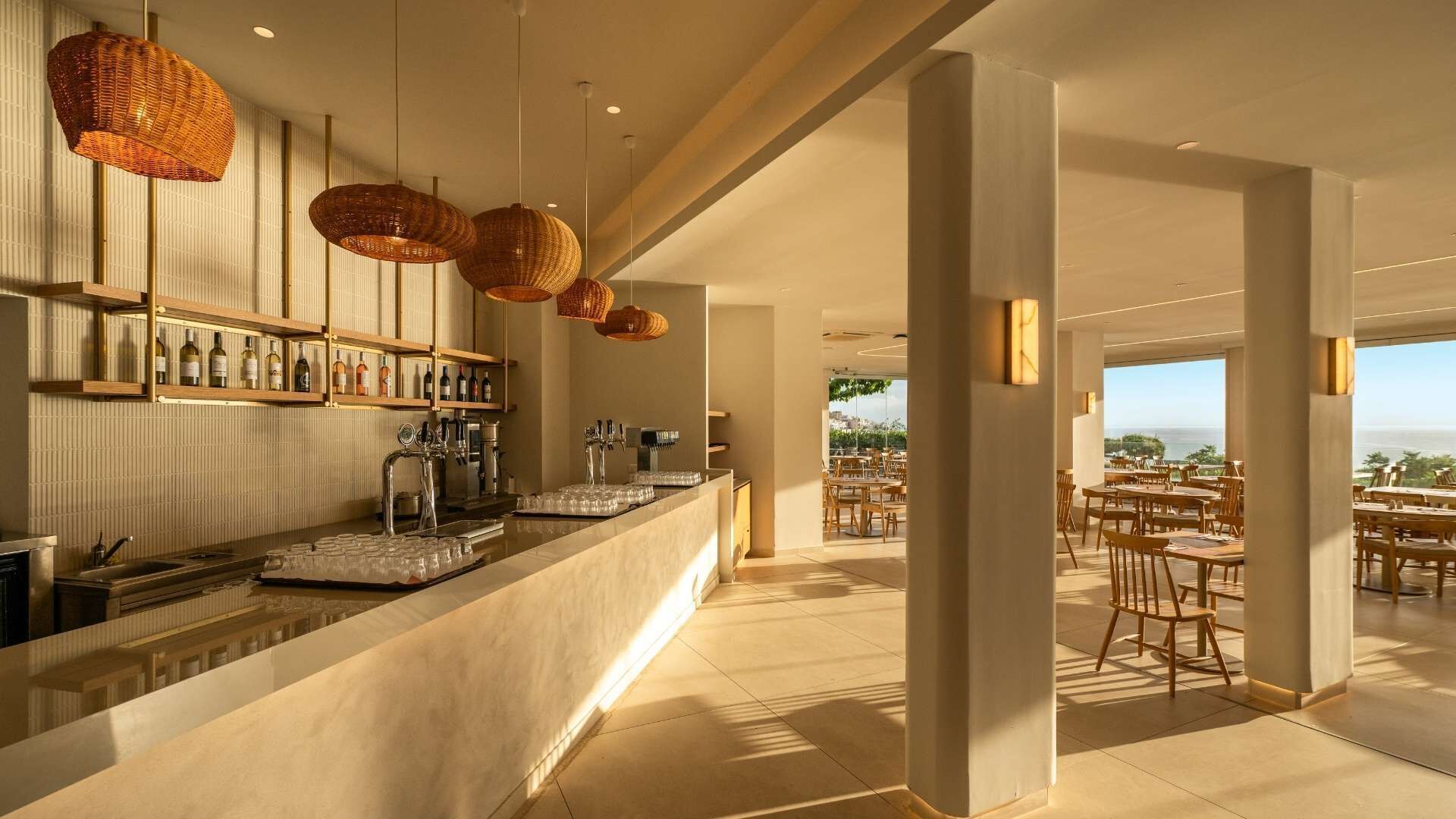 A bar area with a counter, shelves with bottles, and hanging wicker lamps.